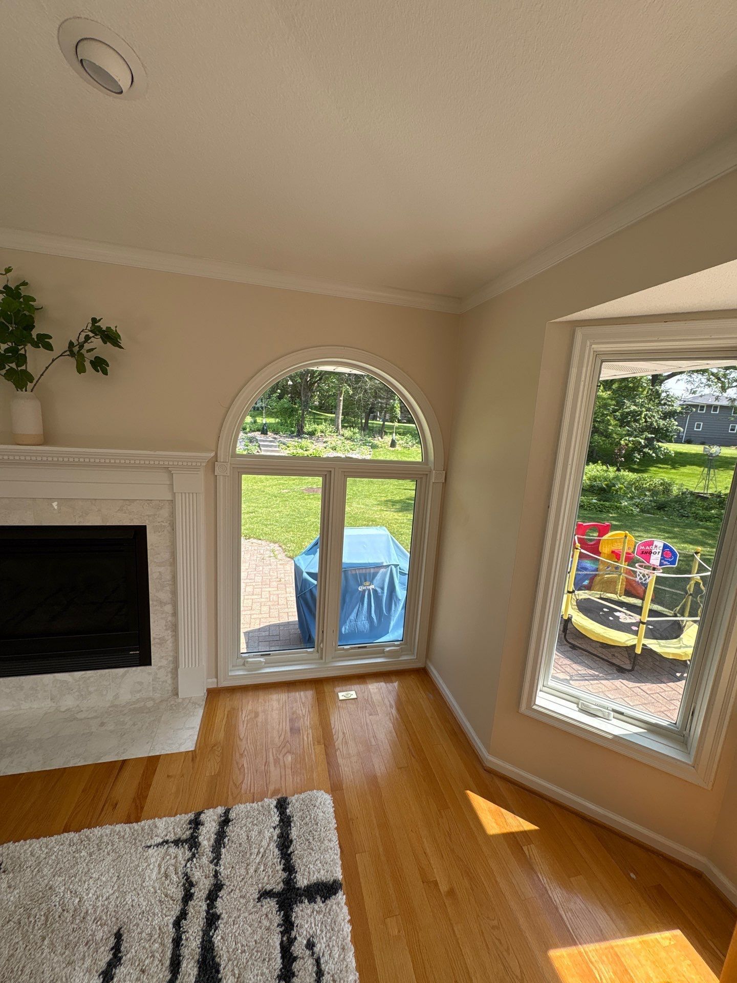Living room with fireplace, arched window and a view of backyard with playset.