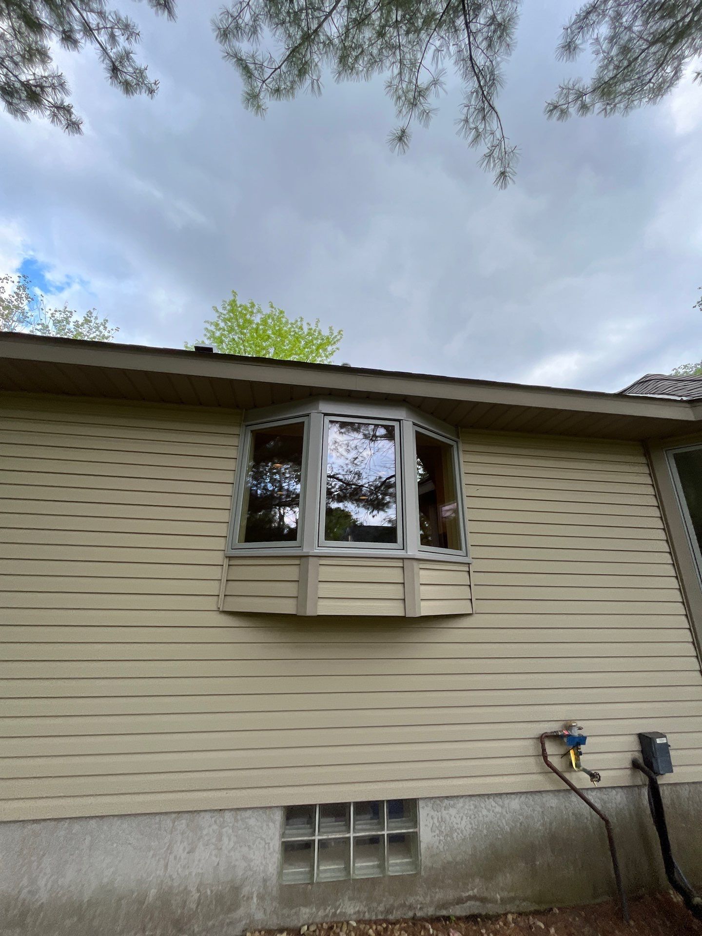 Exterior of a house with a bay window, tan siding, and a cloudy sky.