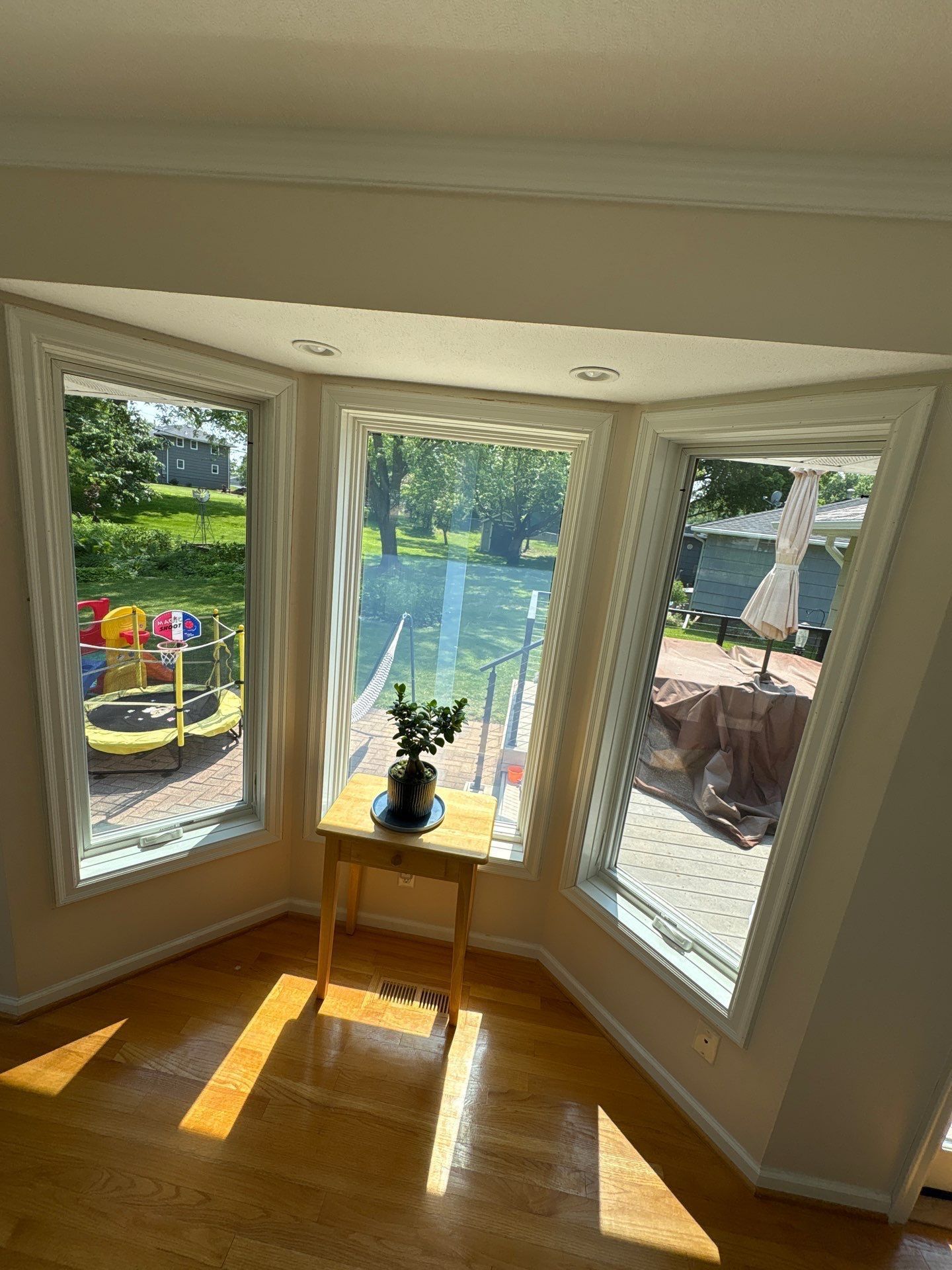 Bay window with a small table and plant inside, overlooking a yard with a playground.
