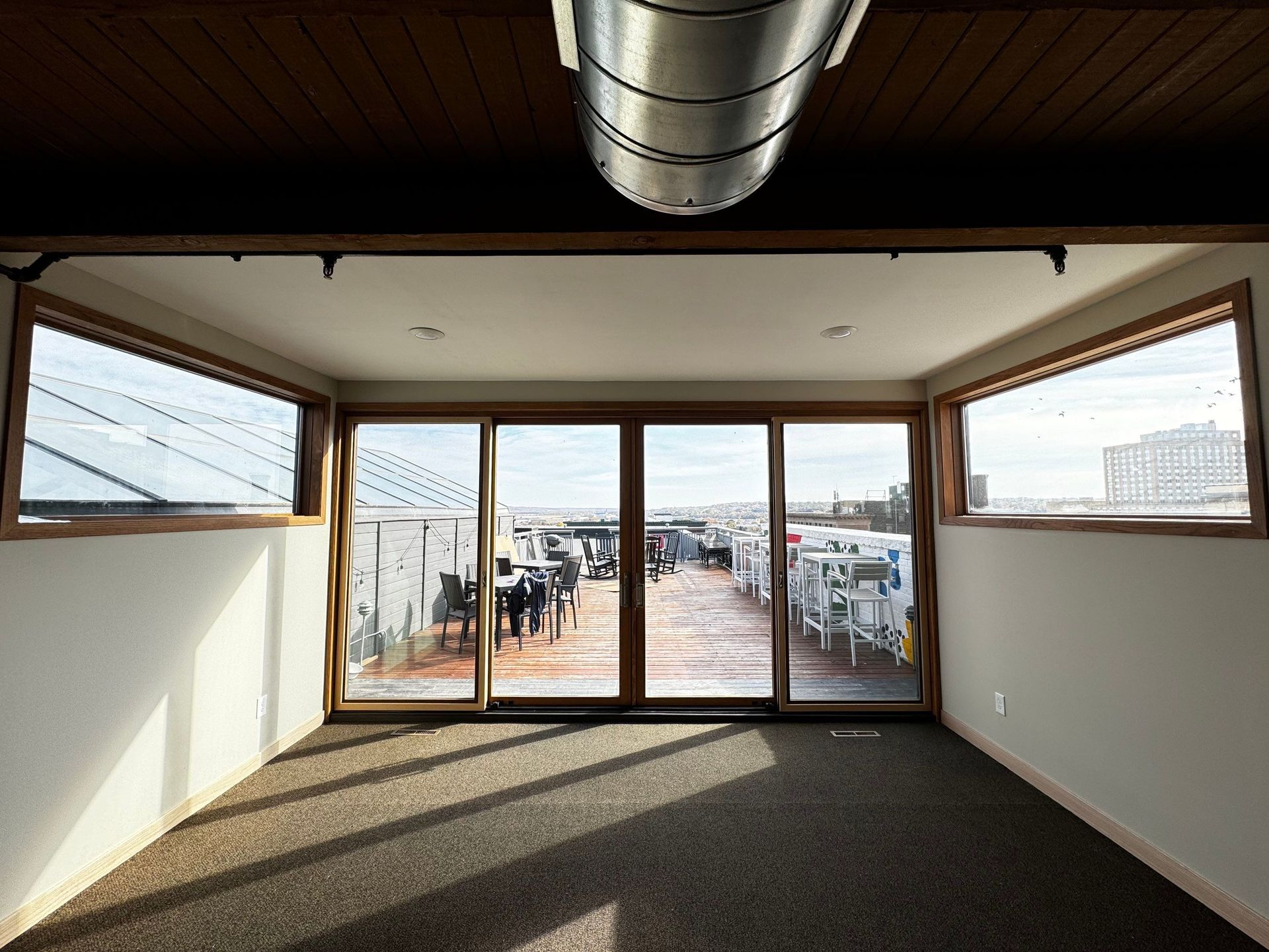 Empty room with windows overlooking a parking area; wood trim, carpet floor, and overhead vent.
