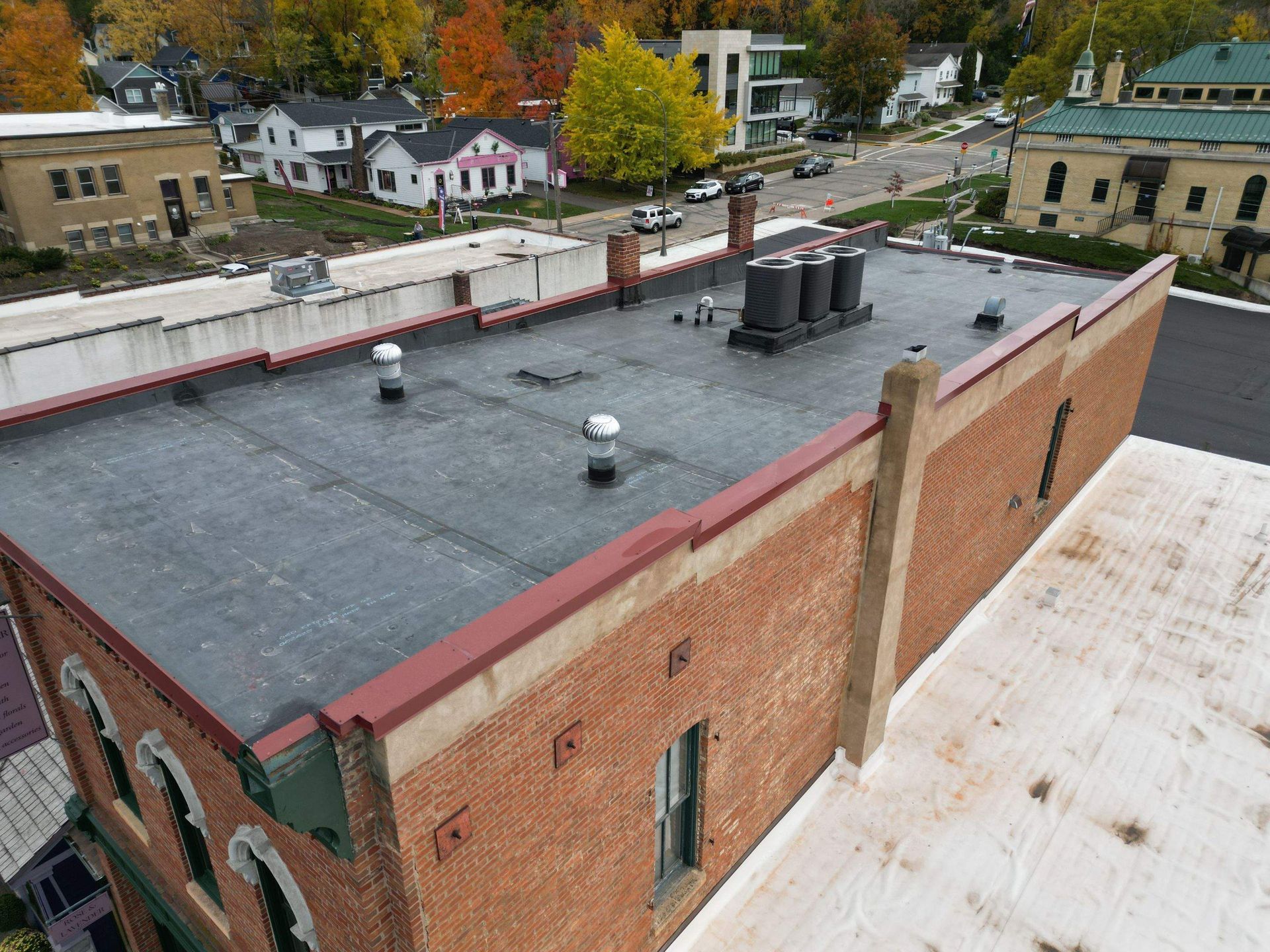 Brick building with a flat roof, venting equipment, and surrounding colorful trees.