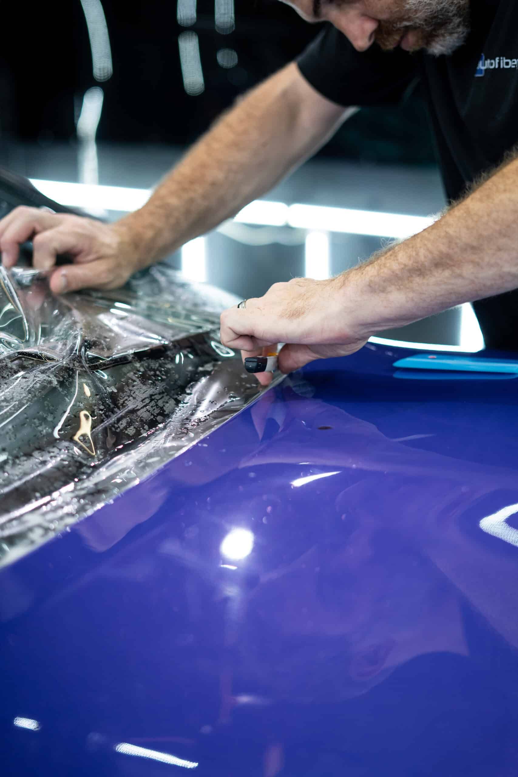 A man is wrapping the hood of a blue car with plastic wrap.