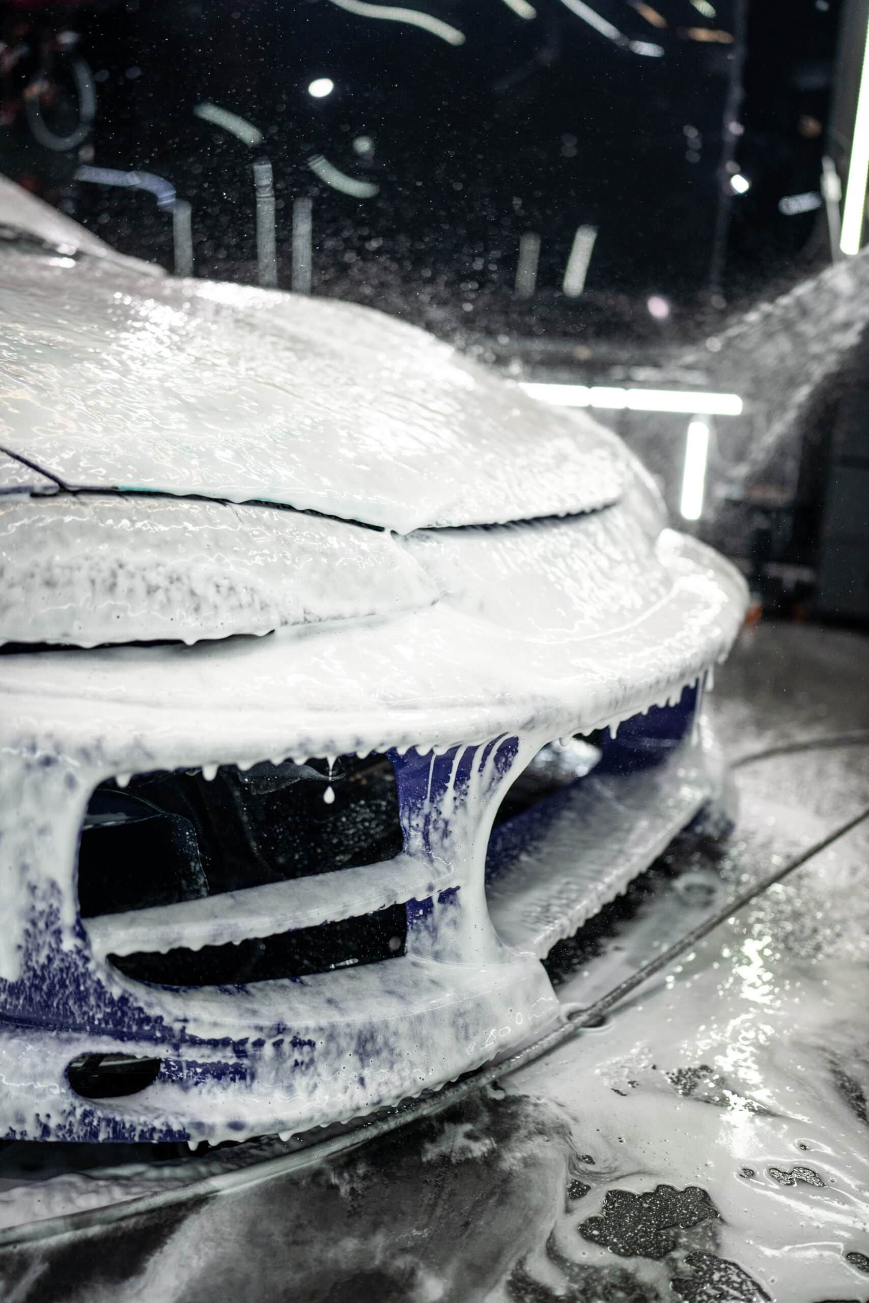 A white car is covered in foam at a car wash.