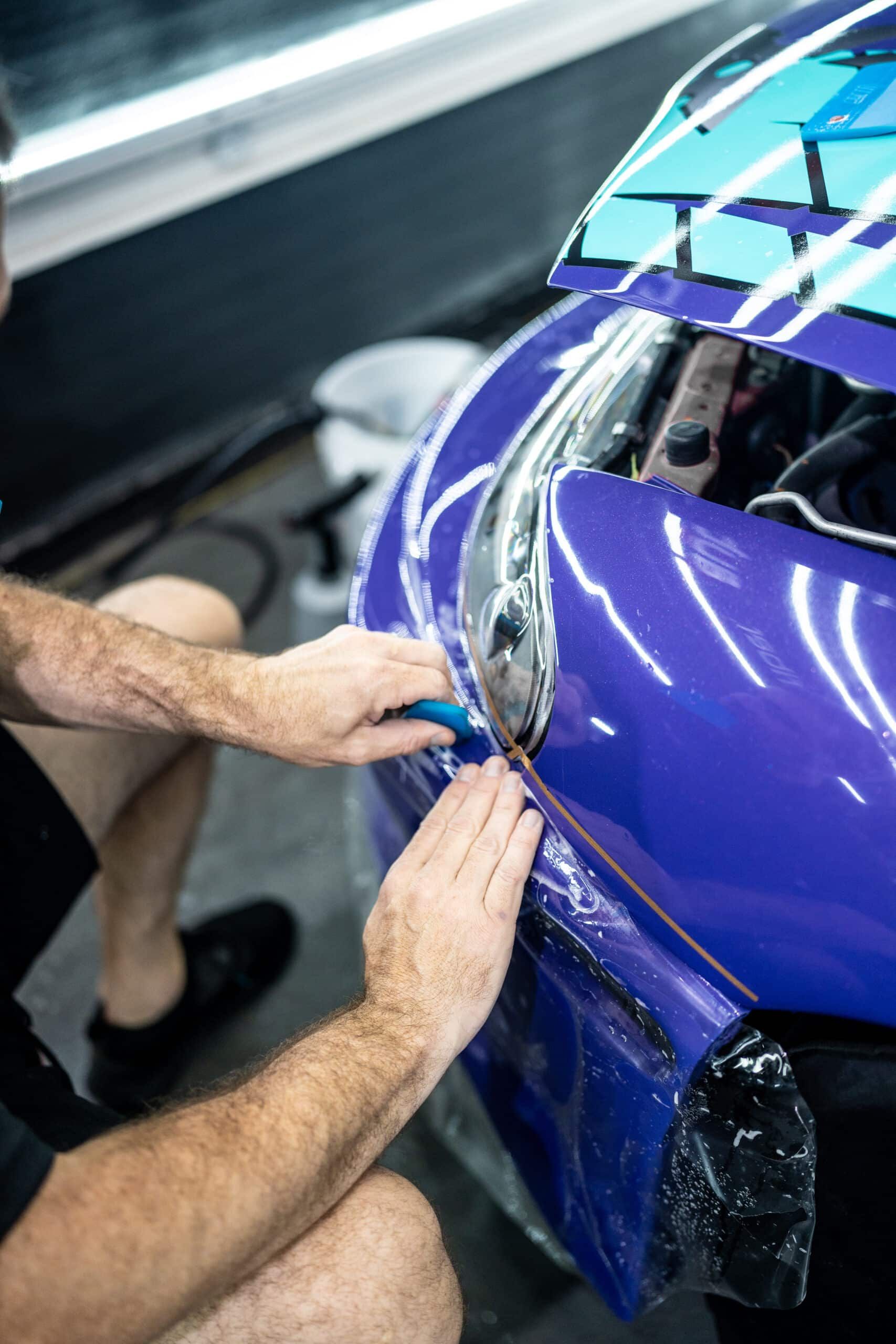 A man is wrapping a purple car with plastic wrap.