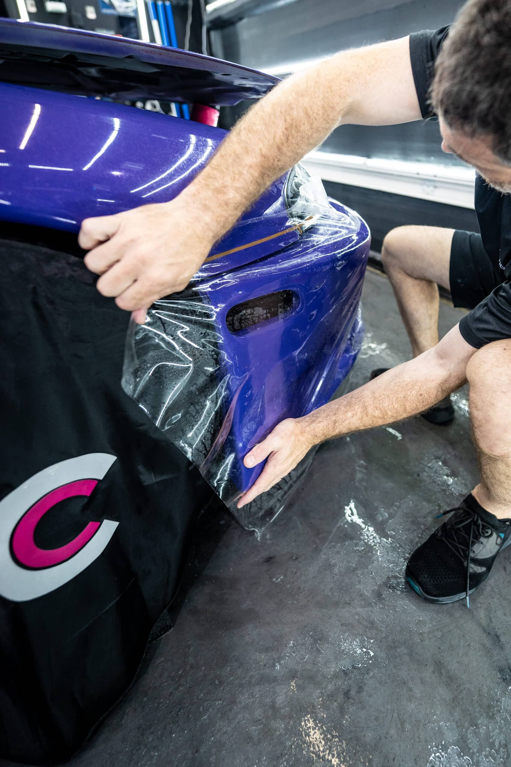 A man is wrapping a purple car with plastic wrap.
