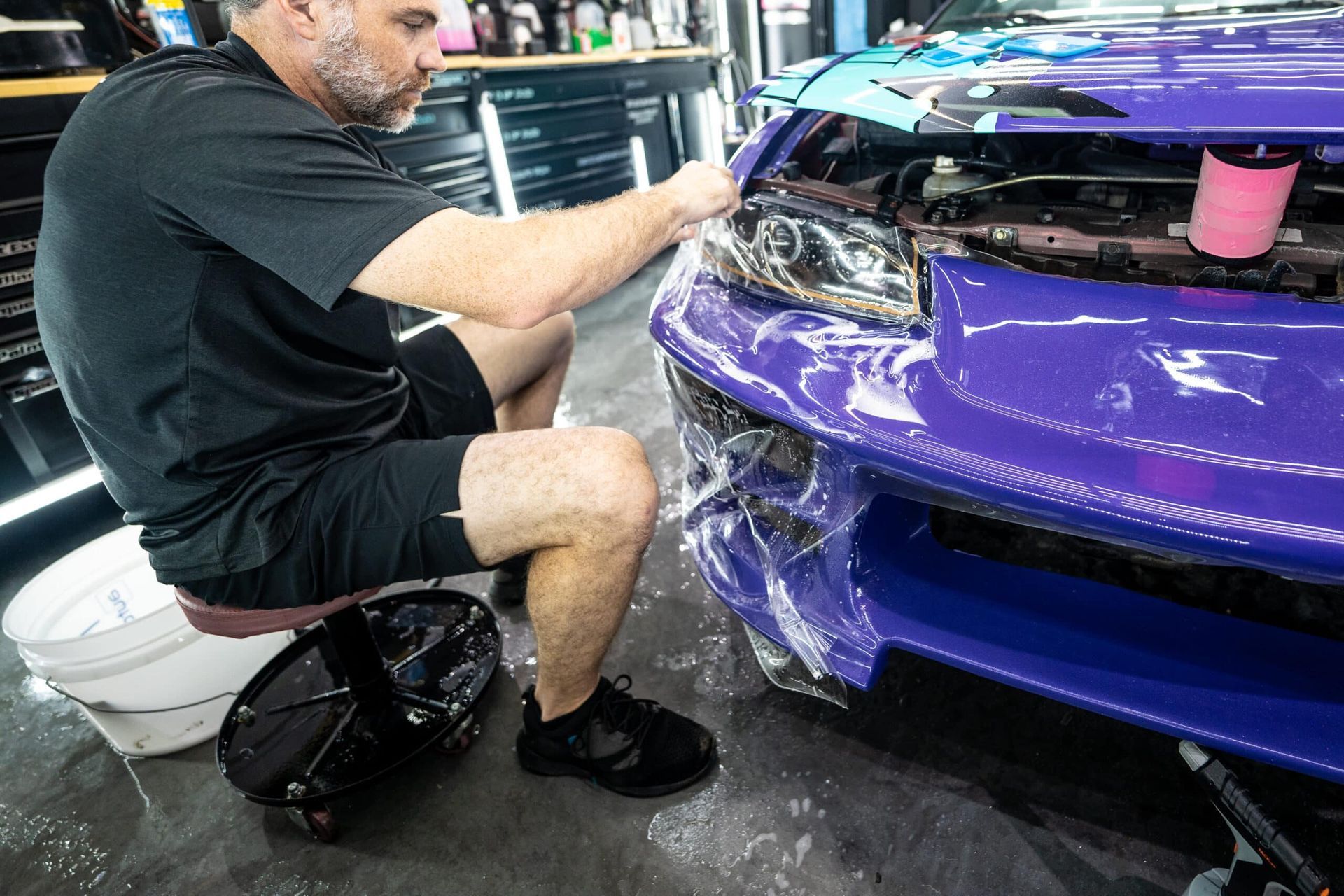 A man is sitting on a stool wrapping a purple car.