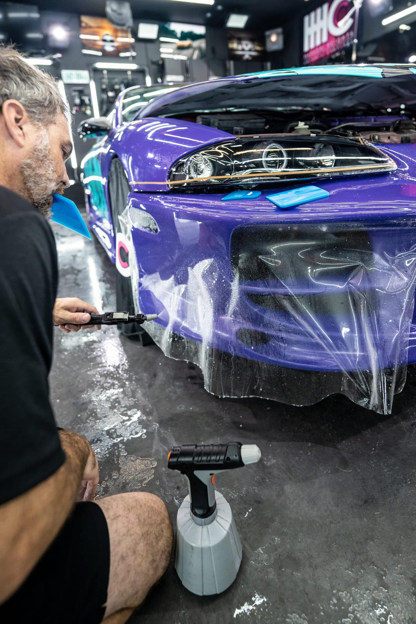 A man is wrapping a purple car with plastic wrap.