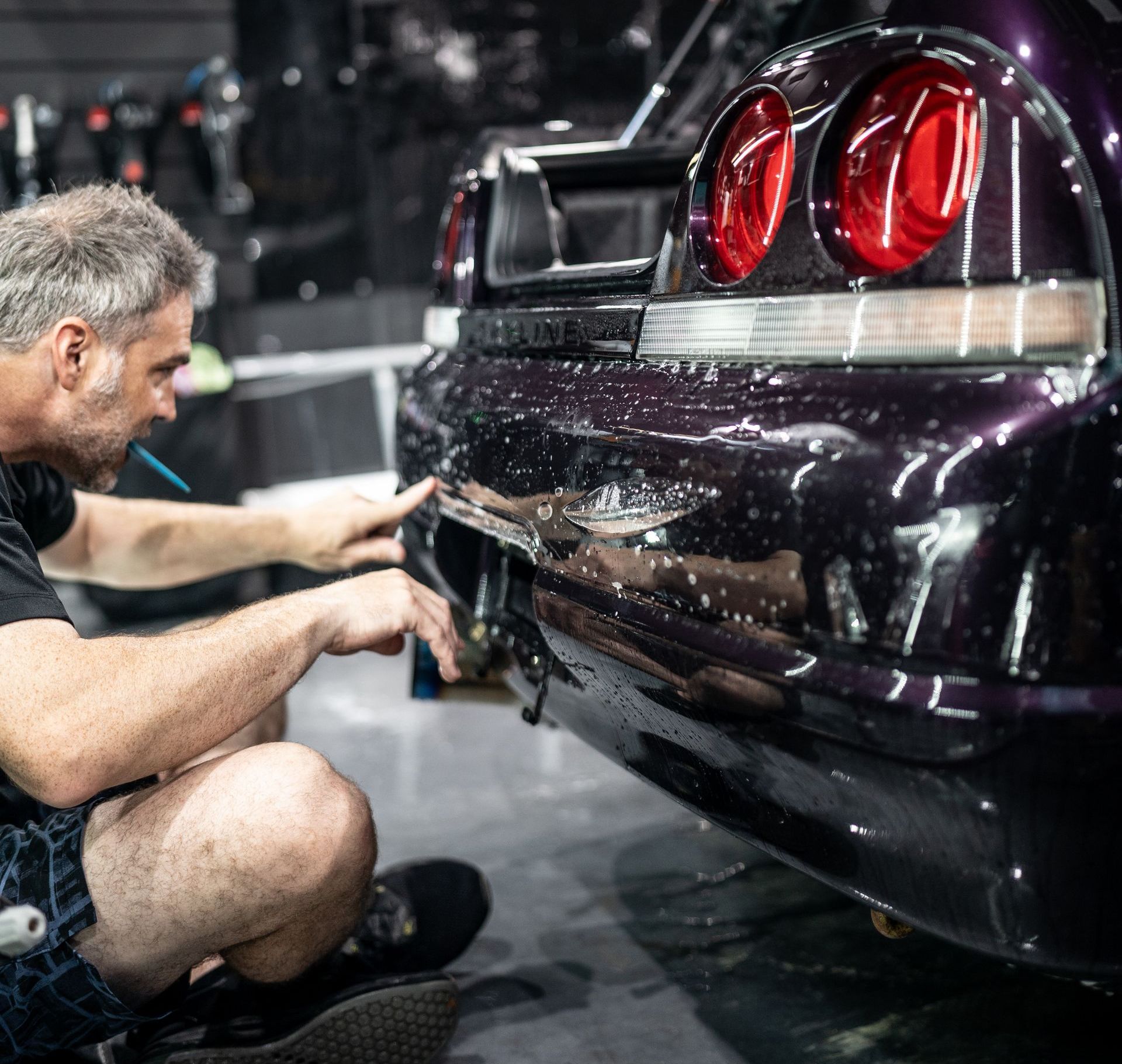 A man is kneeling down next to a purple car in a garage.