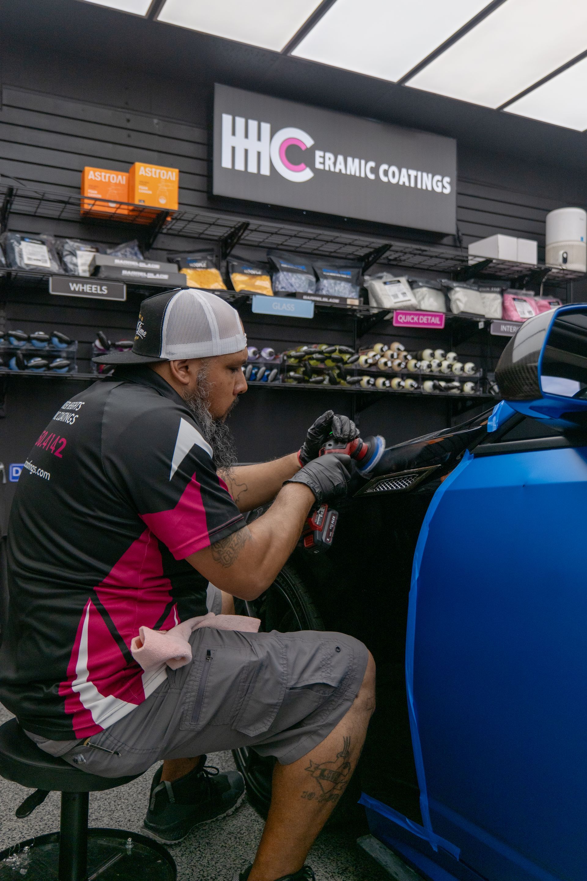 Detailing specialist polishing the front quarter panel of a blue Cadillac CTS-V inside the Harker Heights Ceramic Coatings shop near Temple, TX.