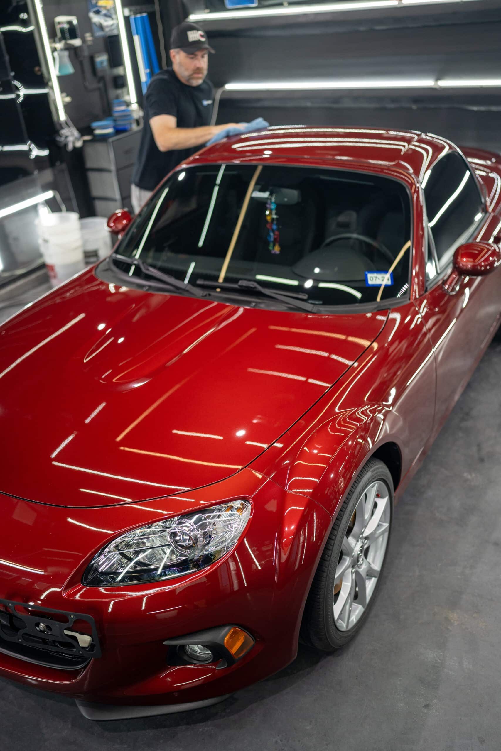 A man is standing next to a red sports car in a garage.