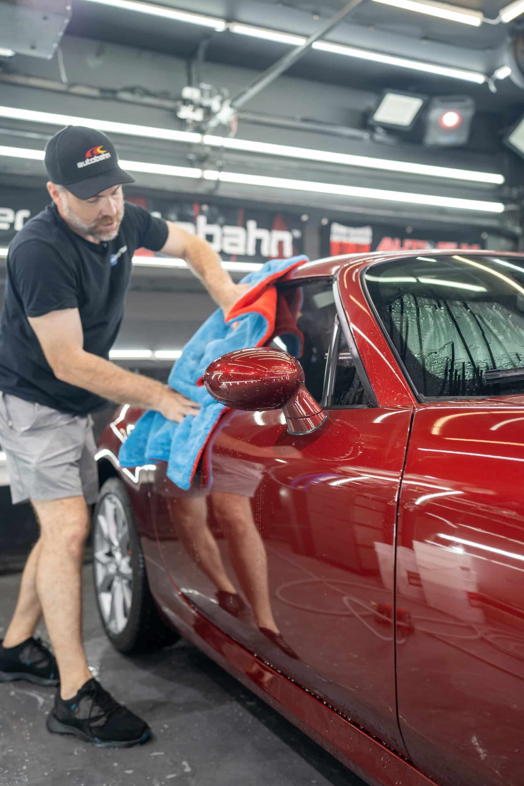 A man is cleaning a red car with a towel.