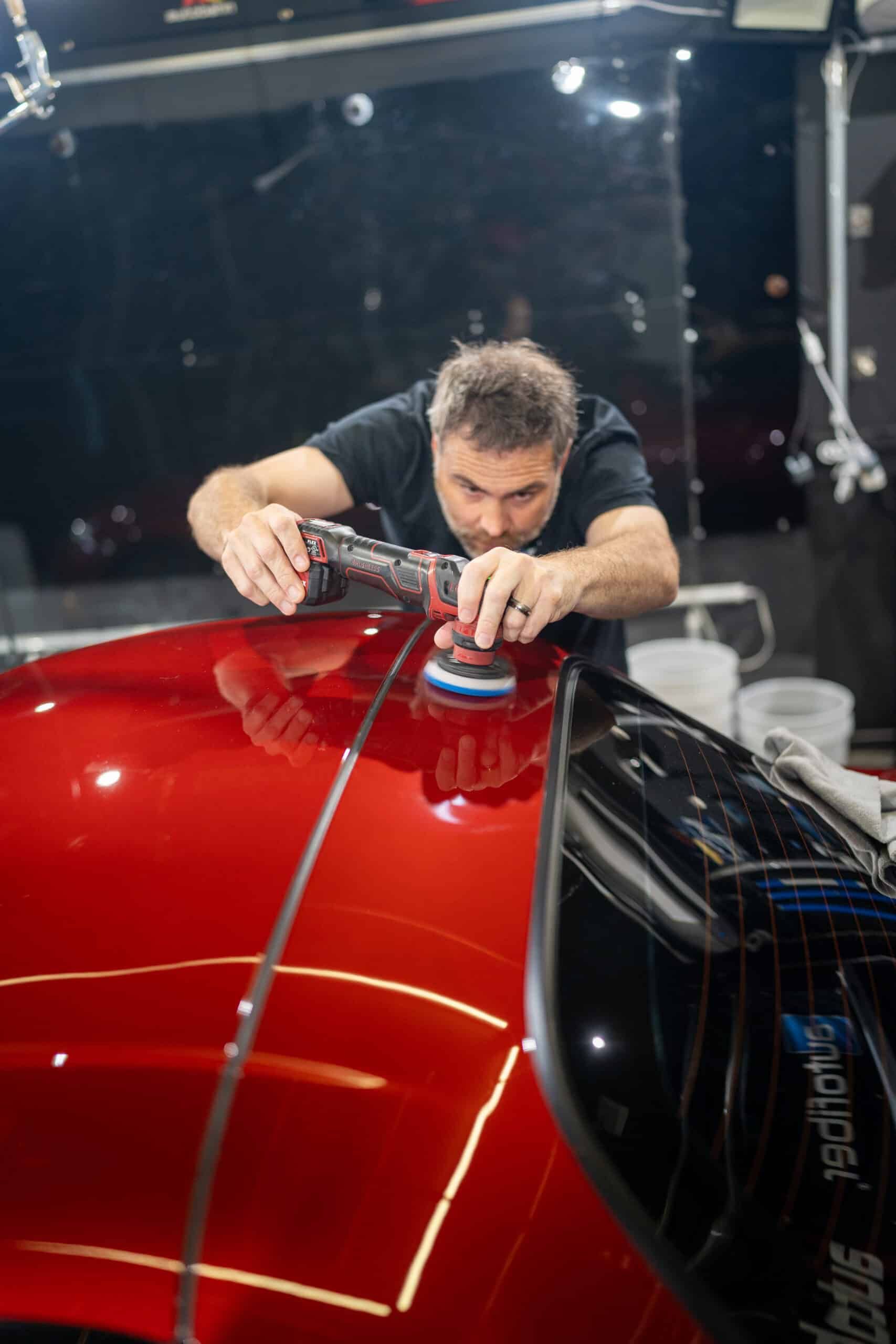 A man is polishing the hood of a red car.