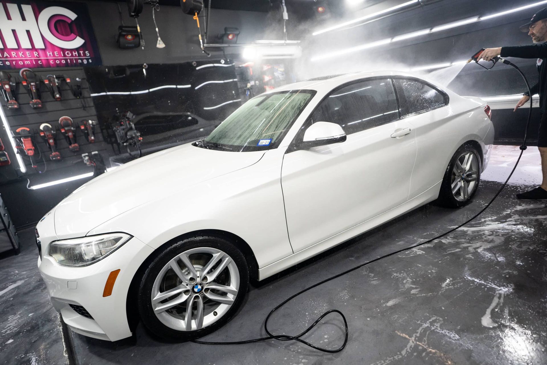 A man is washing a white bmw with a high pressure washer.