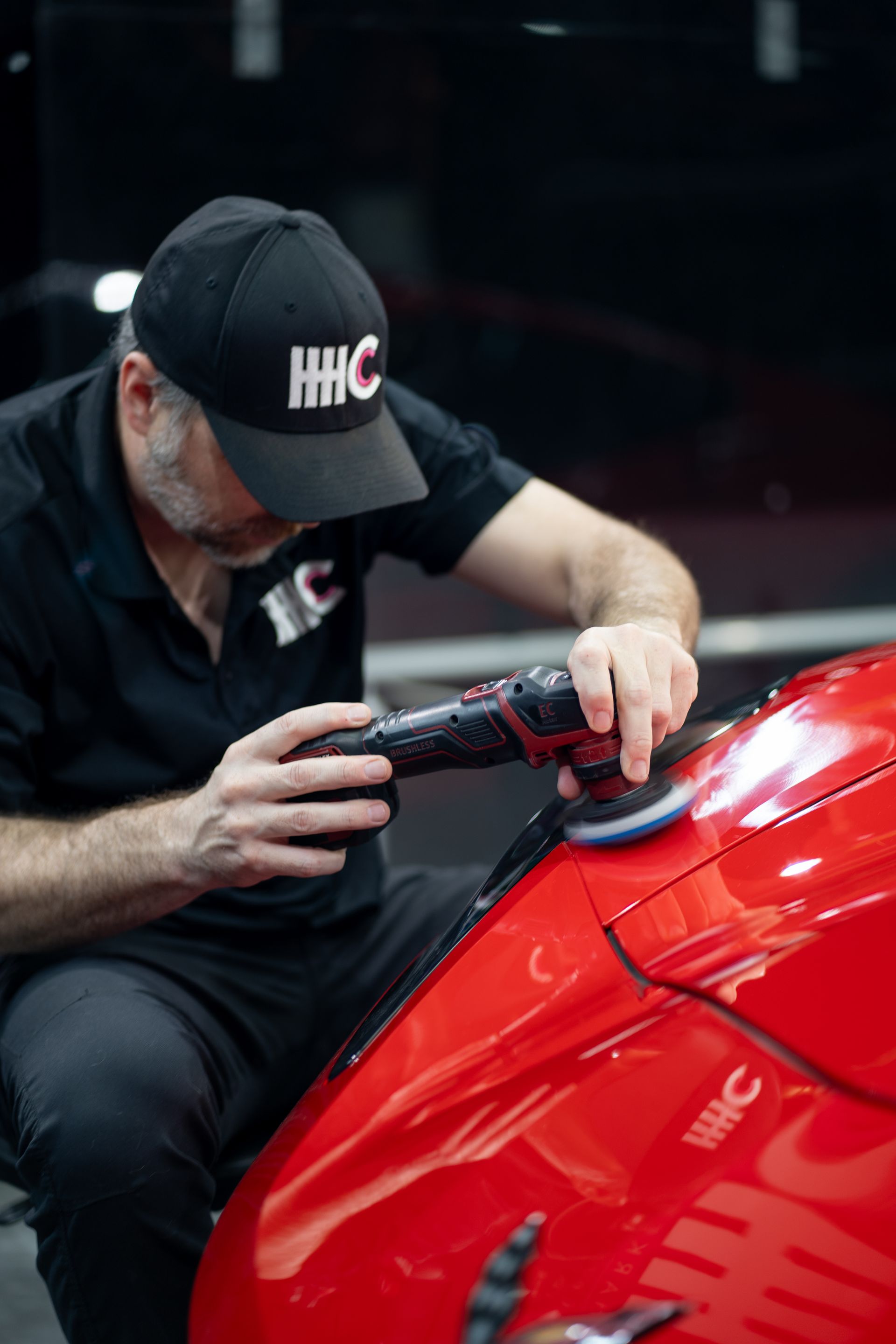 A man is polishing a red car with a polisher.