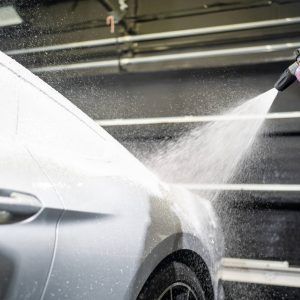 A person is spraying water on a car with a hose.