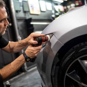 A man is polishing the fender of a car with a polisher.