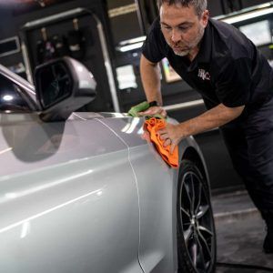 A man is cleaning a silver car with an orange cloth.