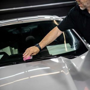 A man is cleaning the windshield of a car with a pink sponge.