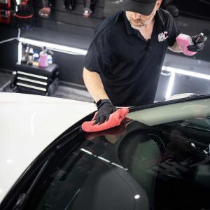 A man is cleaning the windshield of a car with a cloth.