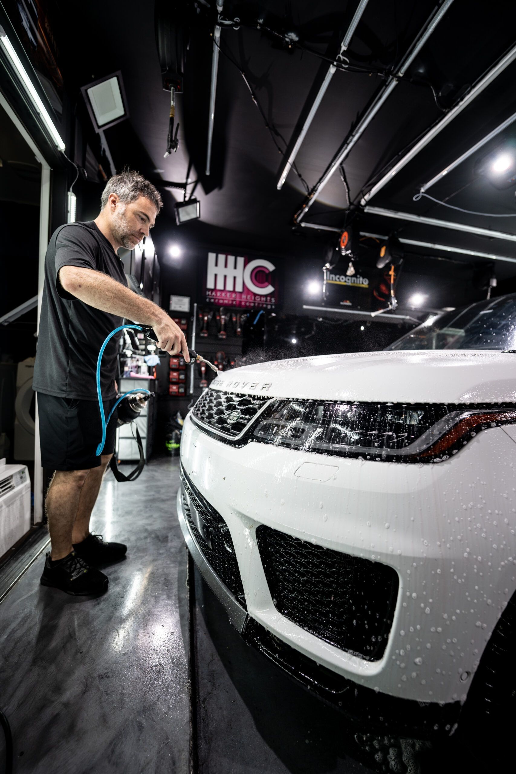 A man is washing a white range rover sport in a garage.