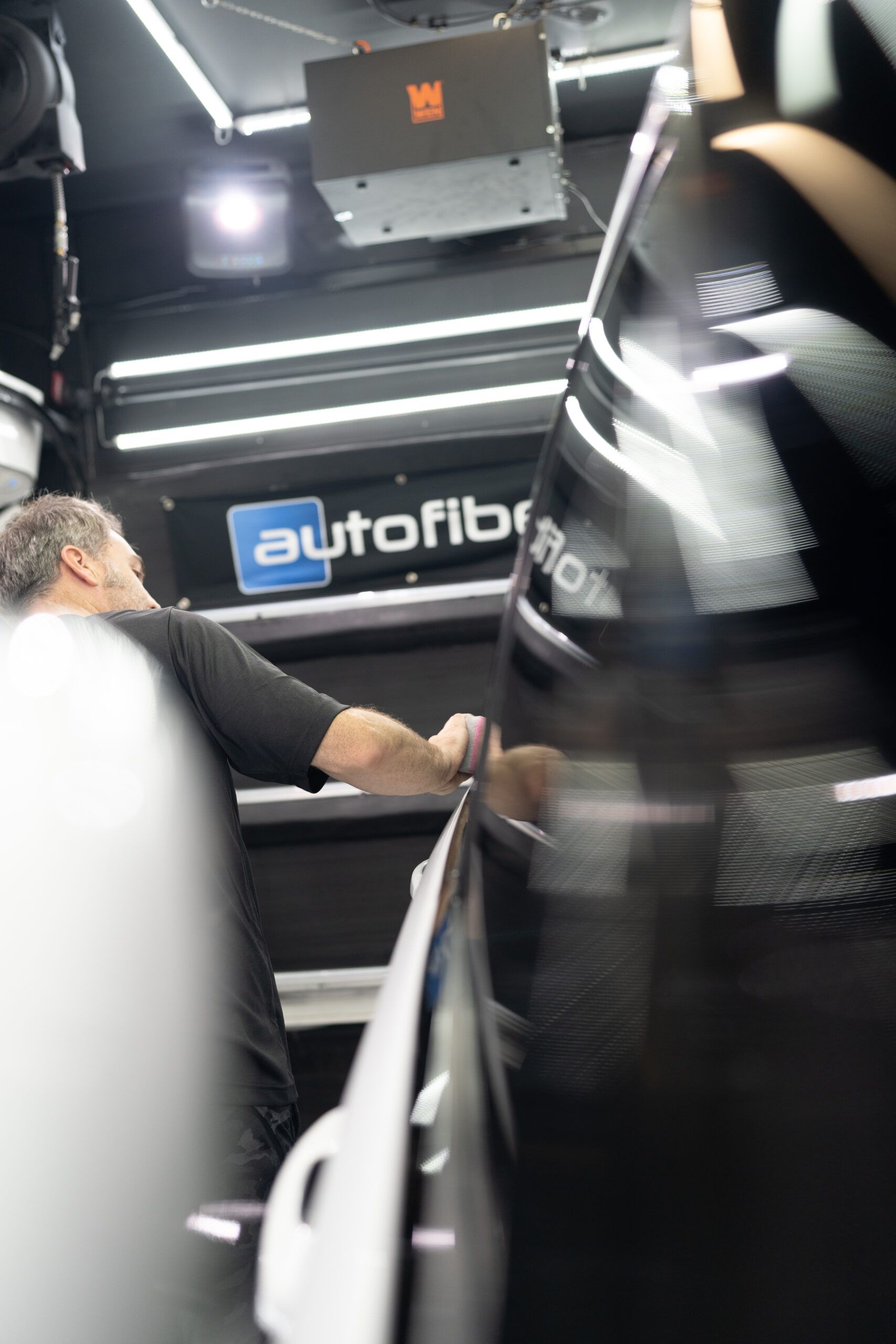 A man is working on a car in front of a sign that says autofiber