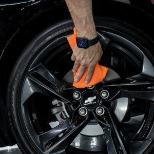 A person is cleaning a car wheel with an orange cloth.