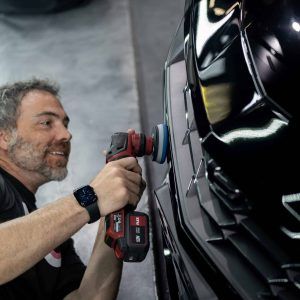A man is polishing a black car with a polisher.