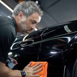 A man is cleaning a black car with an orange towel.