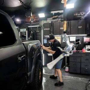 A man is polishing the fender of a truck in a garage.