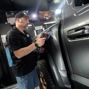 A man is polishing the side of a truck in a garage.