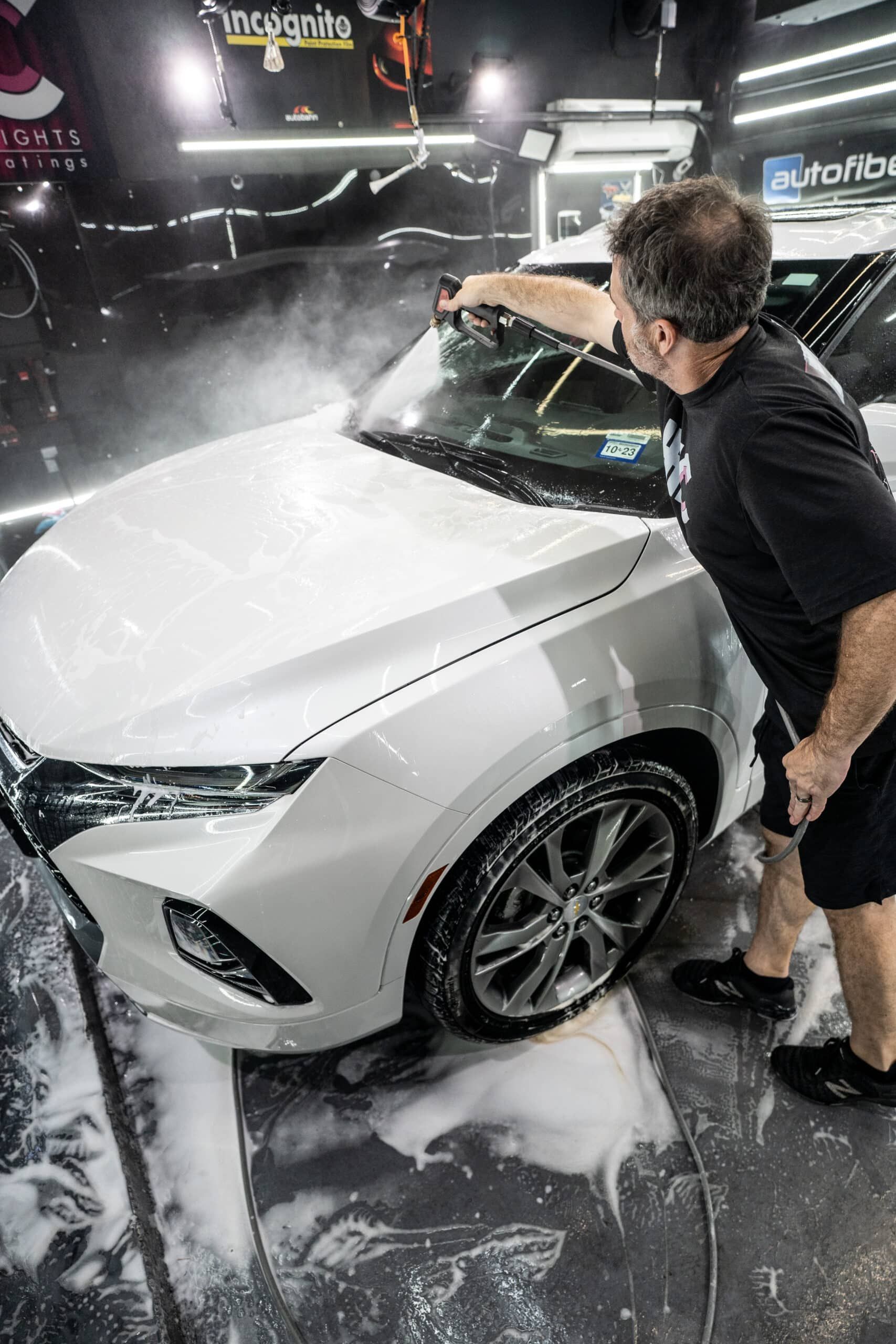 A man is washing a white car in a garage.