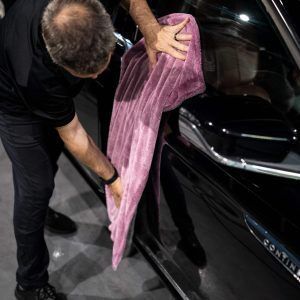 A man is cleaning a black car with a pink towel.