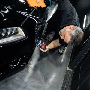 A man is polishing the front of a black car.