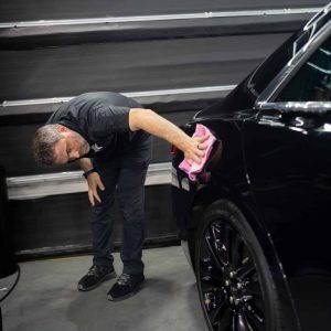 A man is cleaning a black car with a pink cloth.