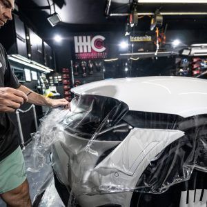 A man is wrapping a white car with plastic in a garage.
