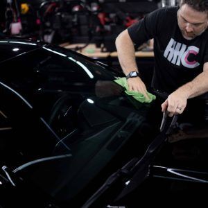 A man is cleaning the windshield of a black car.