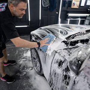 A man is washing a car with a sponge in a garage.