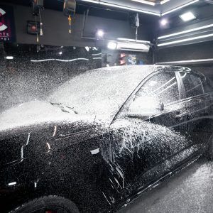 A black car is covered in foam in a garage.