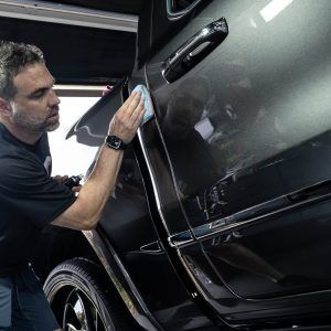 A man is cleaning a black car with a cloth.