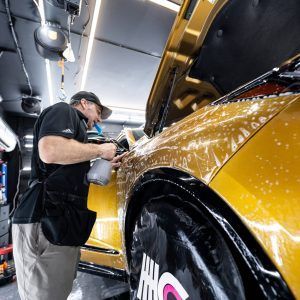 A man is washing a yellow car in a garage.