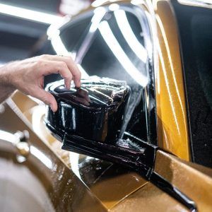 A person is applying a protective film to the side mirror of a car.