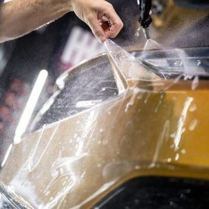 A person is applying a clear plastic film to a car.