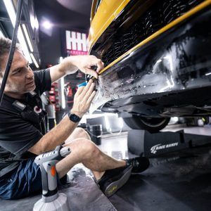 A man is sitting on the floor working on a car.