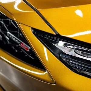 A close up of a yellow car with the headlights on