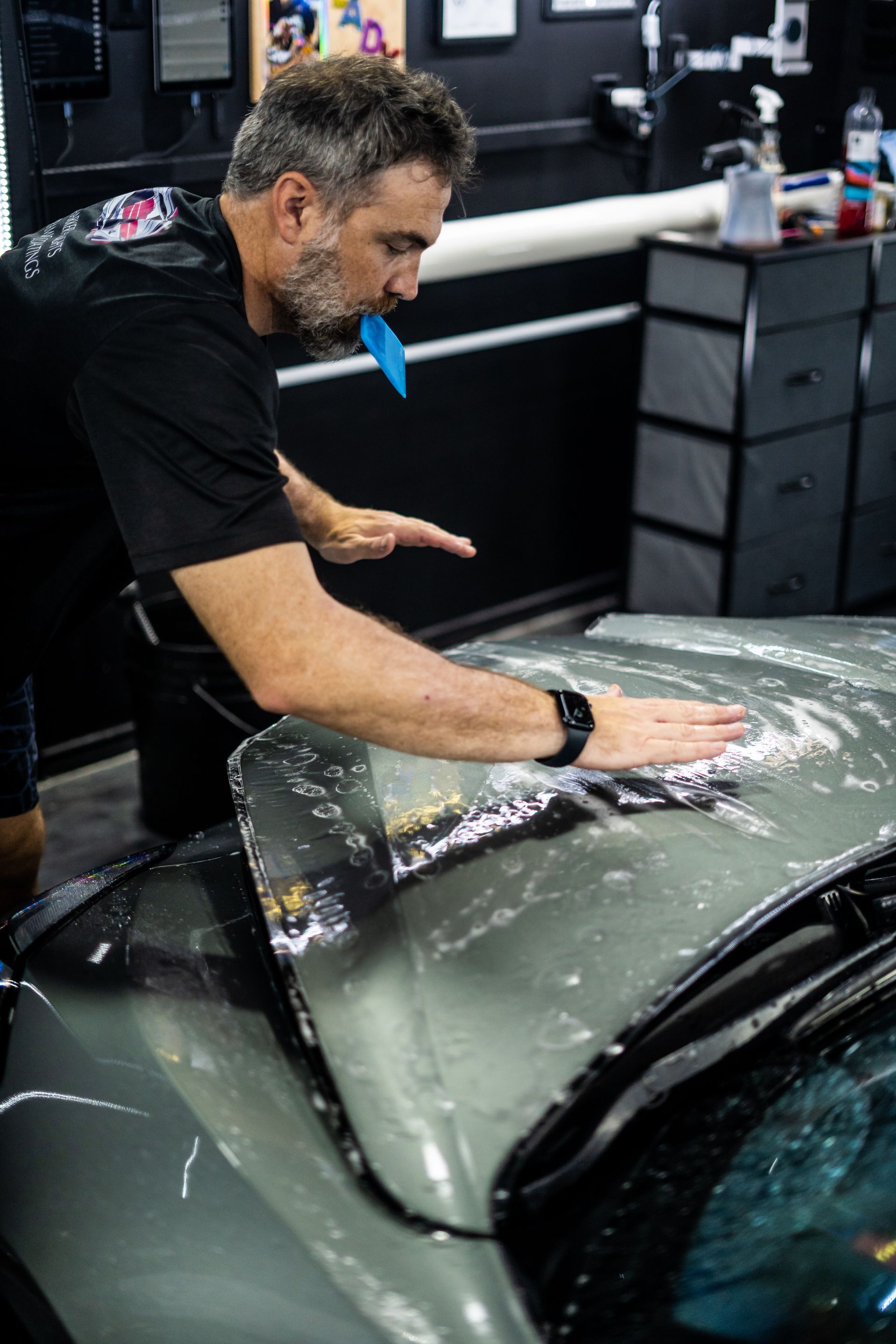 A man is applying a protective film to the hood of a car.