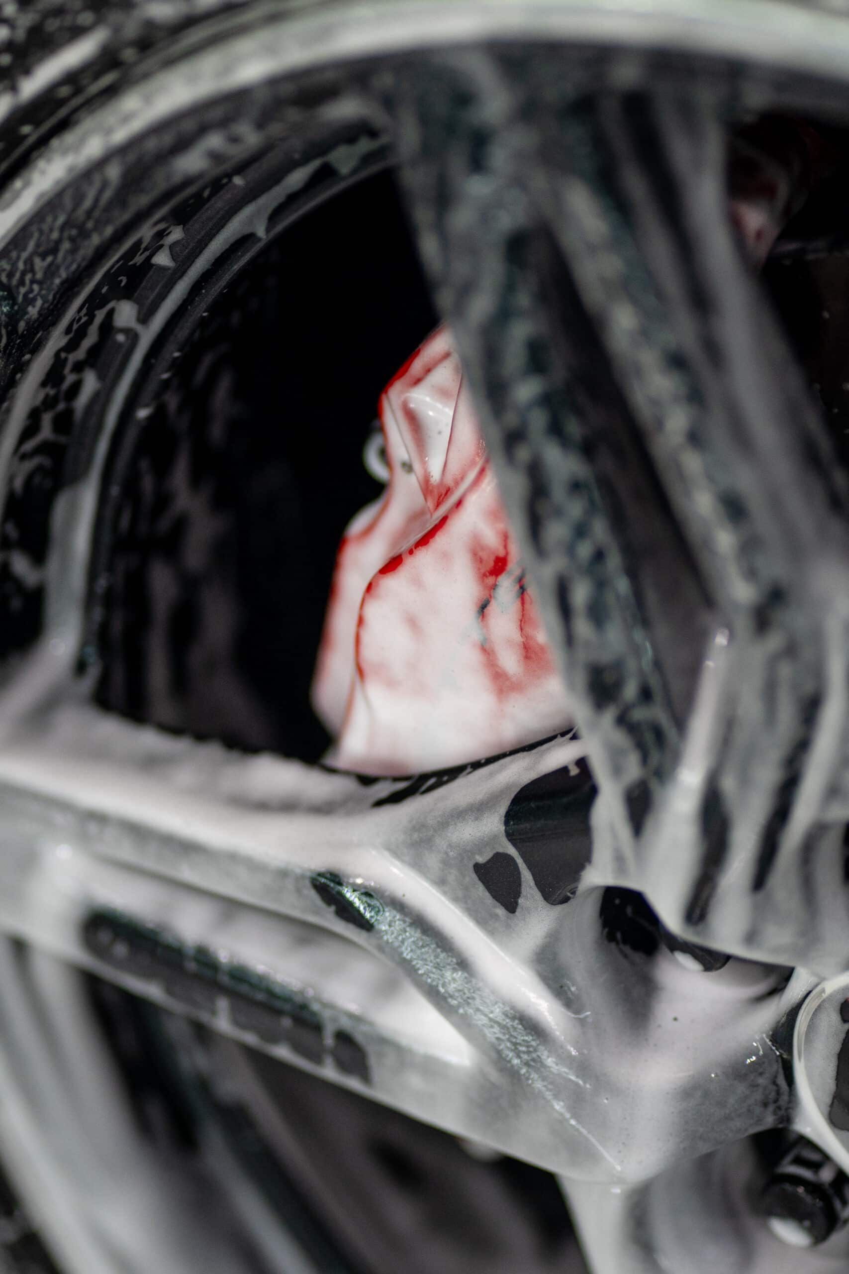 A close up of a car wheel being cleaned with foam.
