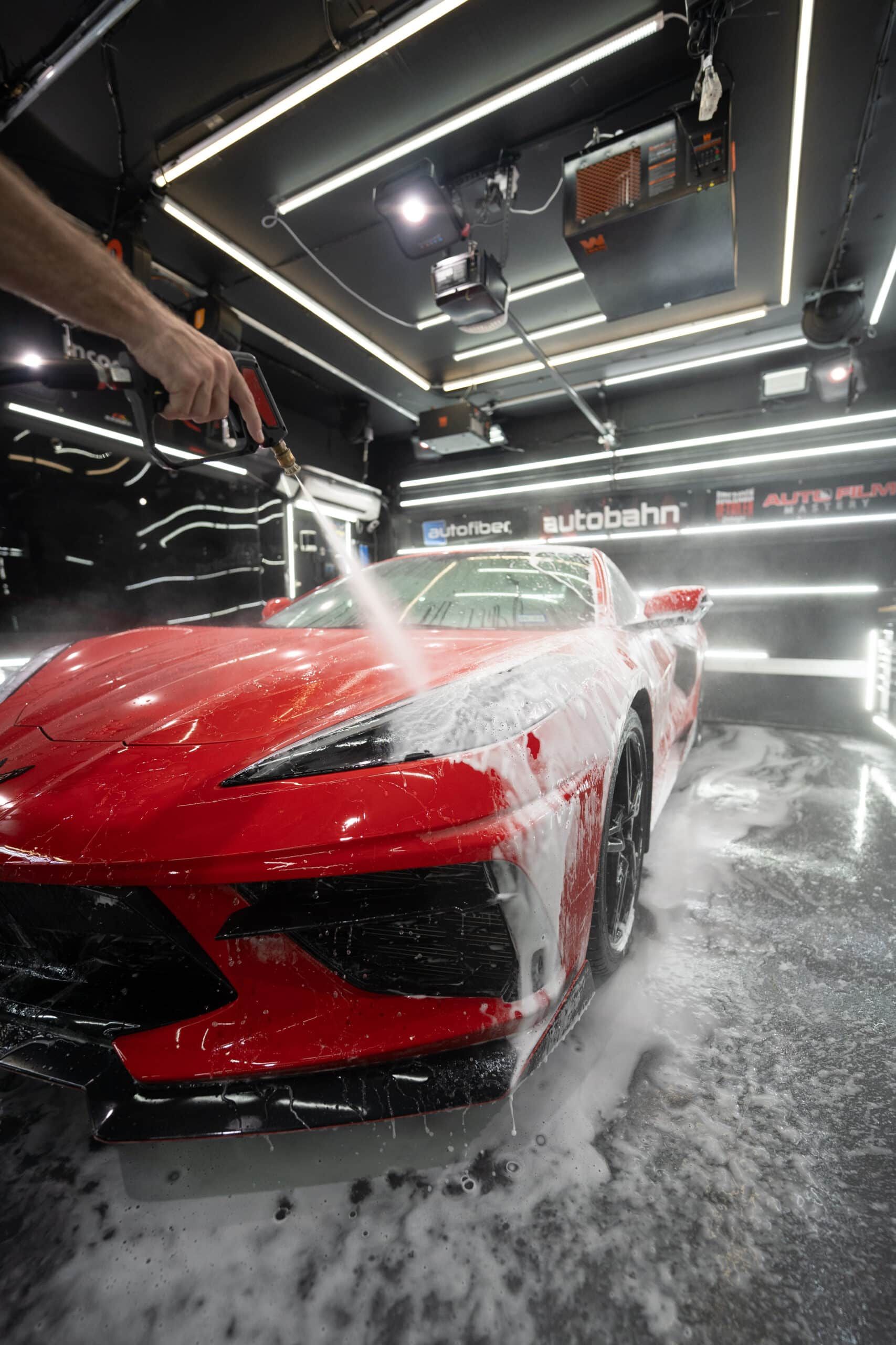 A person is washing a red sports car in a garage.