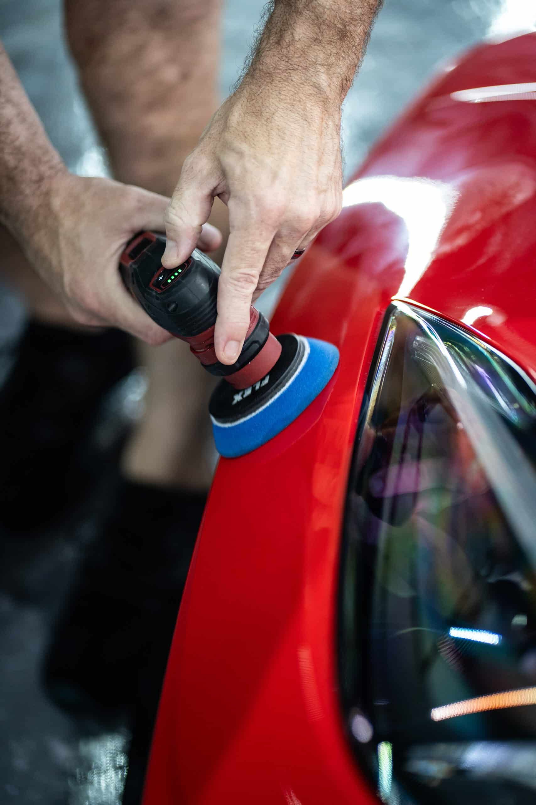 A man is polishing a red car with a polisher.
