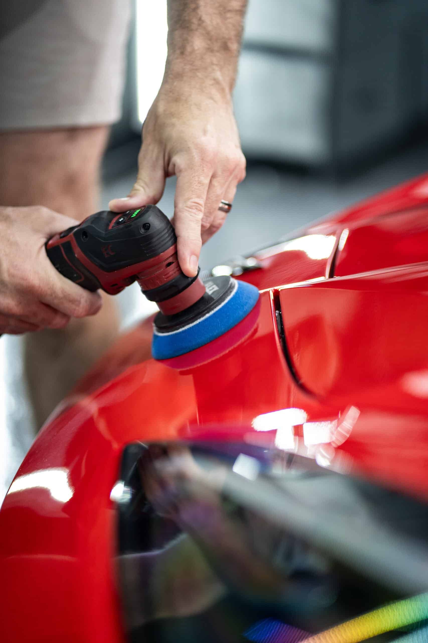 A man is polishing a red car with a machine.