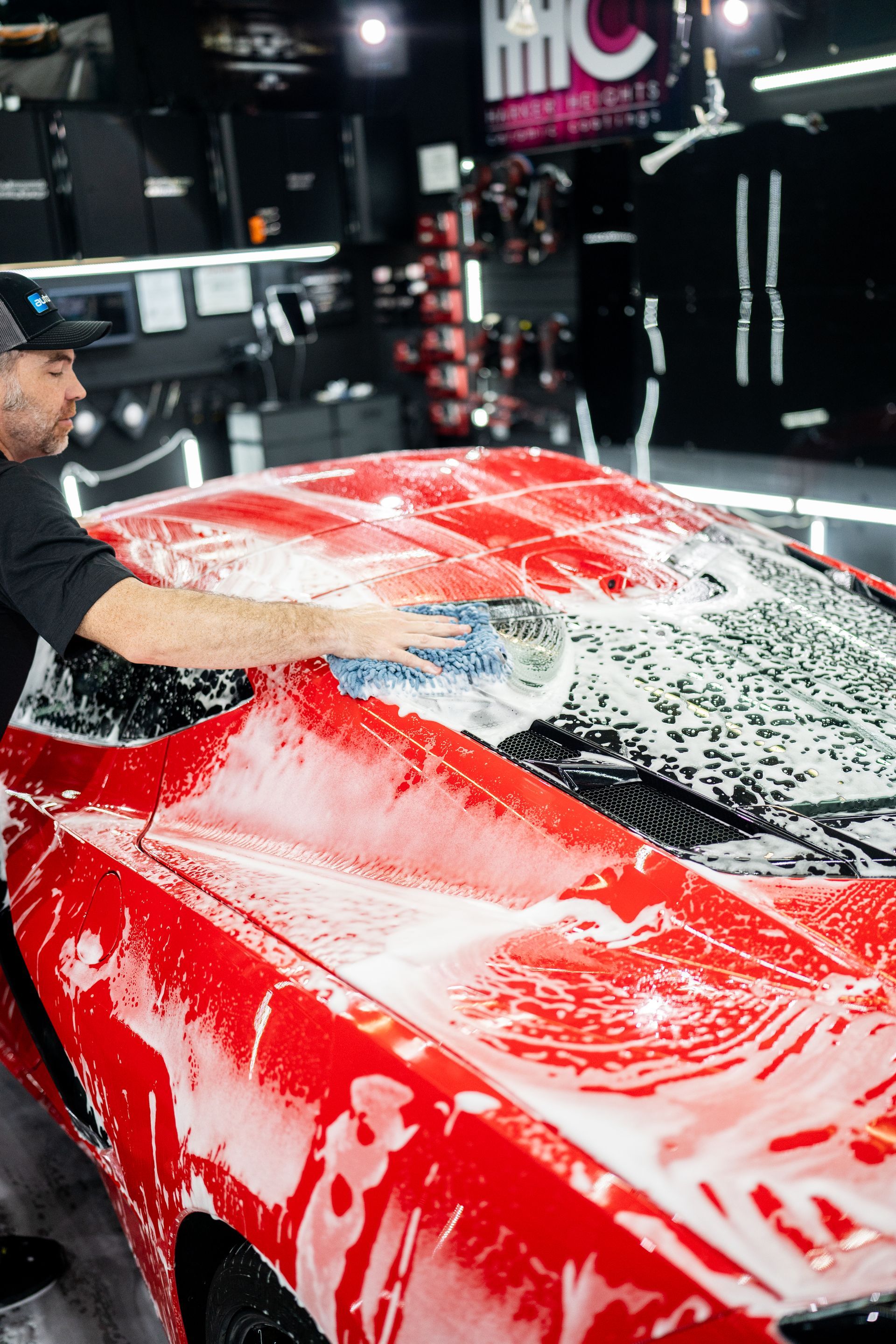 A man is washing a red sports car with soap and water.